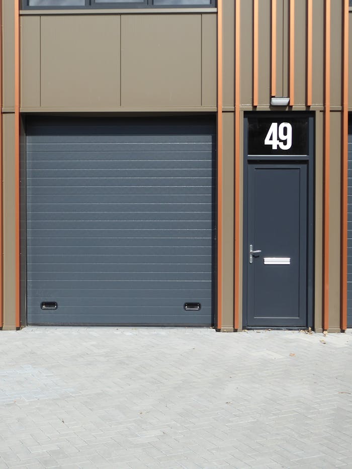 pexels-photo-28384143 A contemporary building facade featuring a dark garage door and entrance with number 49.